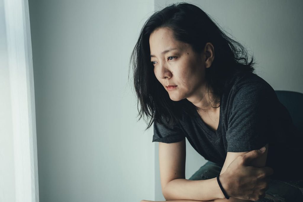 young, anxious looking woman sitting alone and pondering the signs of an adderall addiction