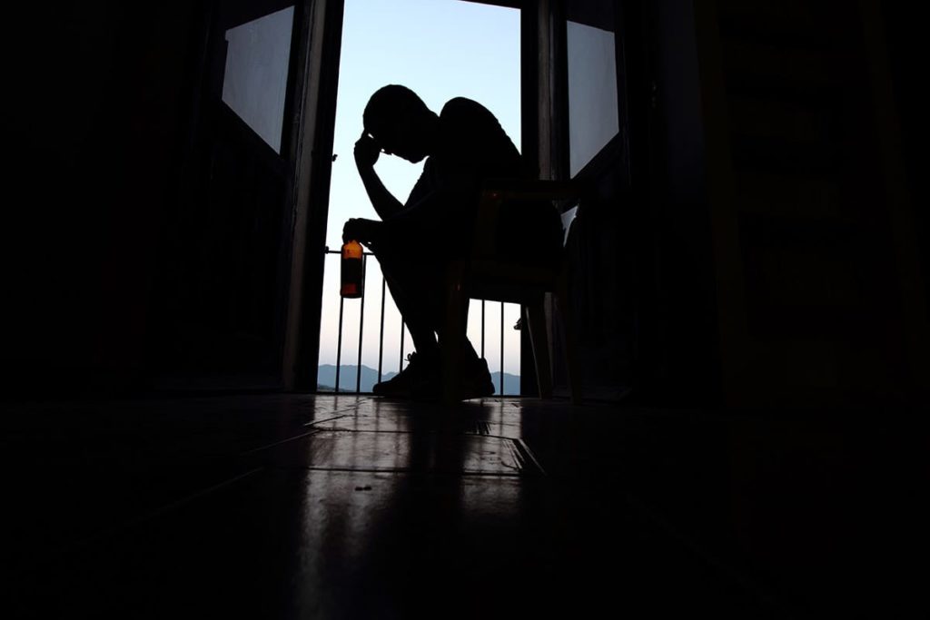 a man hunched over with alcohol in his hand thinking of 5 common signs of alcoholism