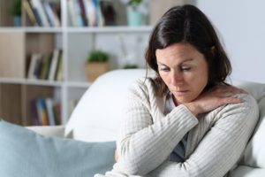 young woman sitting on couch hugging herself and looking distressed experiencing several of the 5 signs of fentanyl overdose