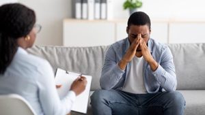 troubled man with face in hands participating in ptsd treatment session with therapist