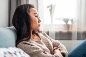 woman sitting on couch deep in thought wondering what are the dangers of opioid use disorder
