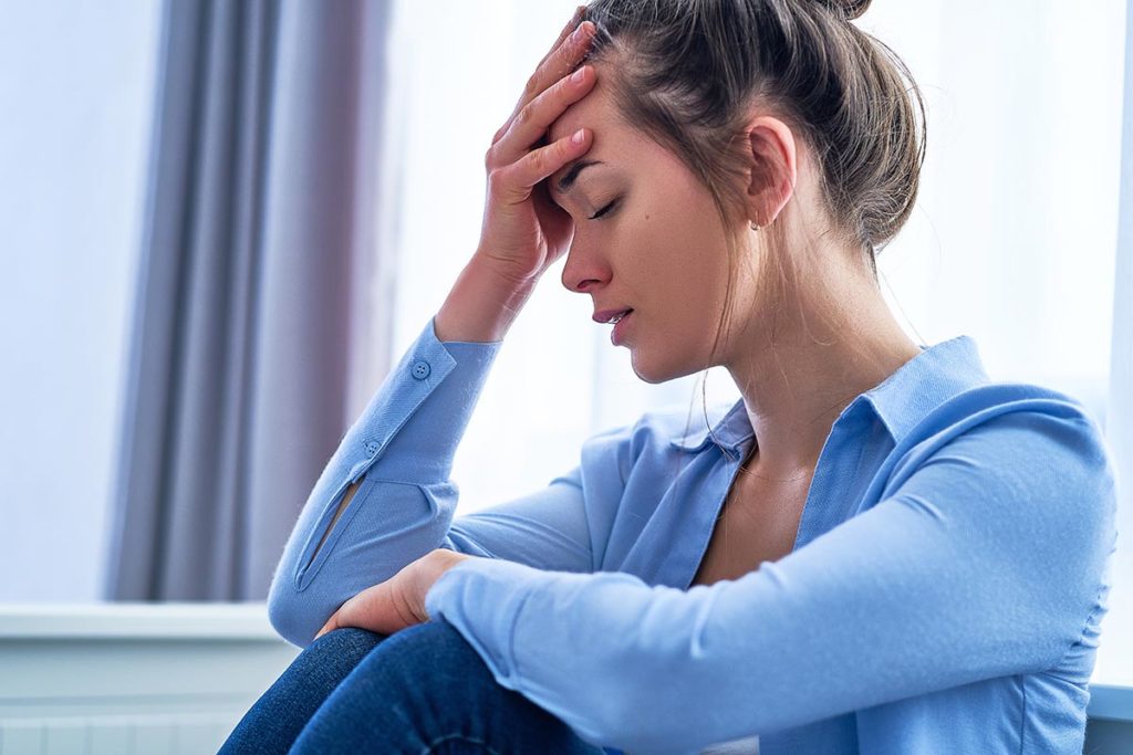 troubled young woman sitting in well lit room with head in her hands wondering what are the types of depression