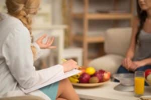 therapist offering nutrition counseling to a client while a bowl of healthy fruit is sitting on the table