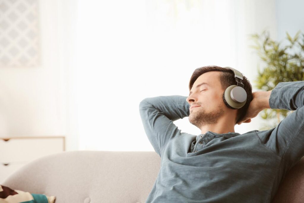 young man relaxing on couch with earphones and enjoying one of the 5 benefits of music therapy