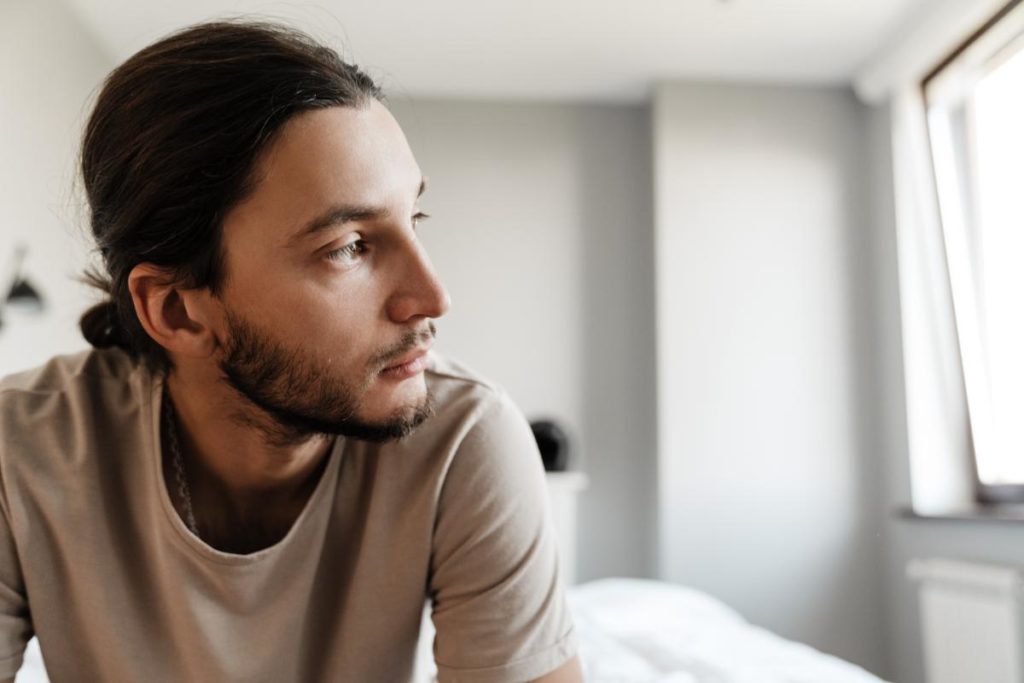 young man sitting alone in bedroom displaying signs you need trauma therapy