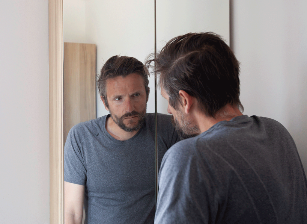 man looking at reflection in mirror asking what are the signs you need trauma therapy