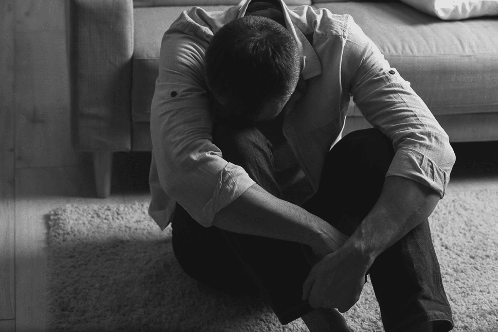 exhausted looking man seated in slumped position on his bedroom floor experiencing one of the 3 long-term effects of cocaine use