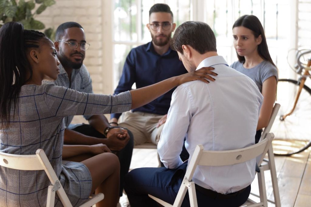 a man is supported and uplifted by his peer recovery support group after his relapse