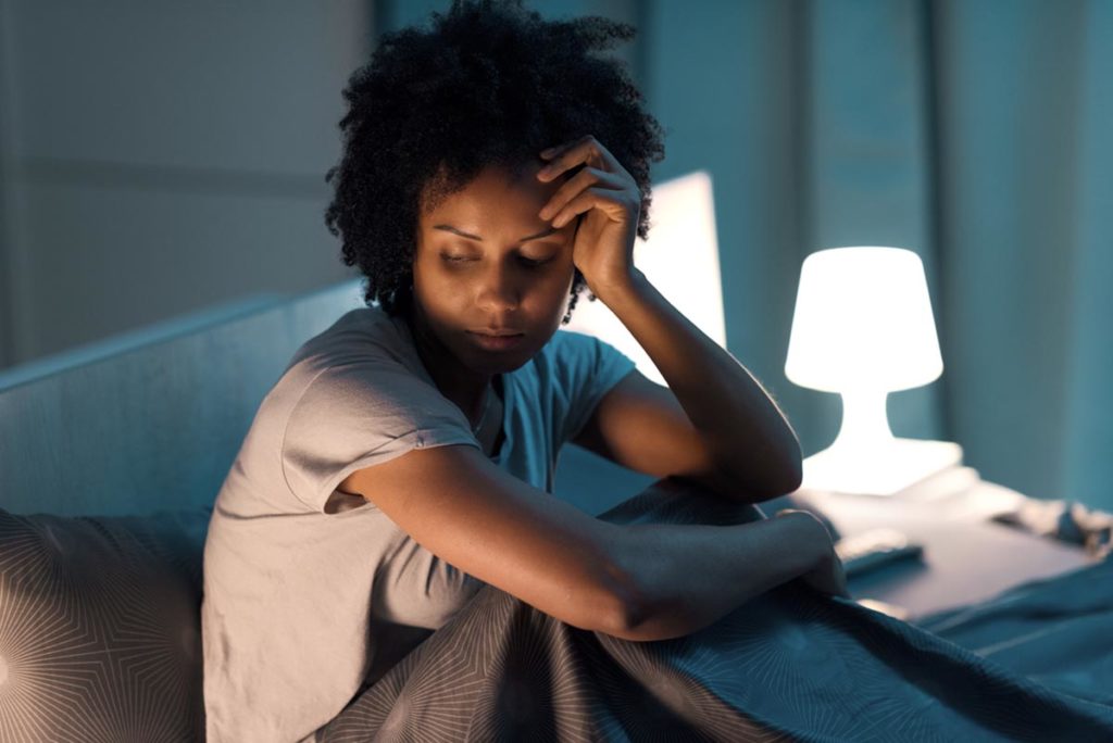 Woman sitting up in bed pondering common causes of alcoholism