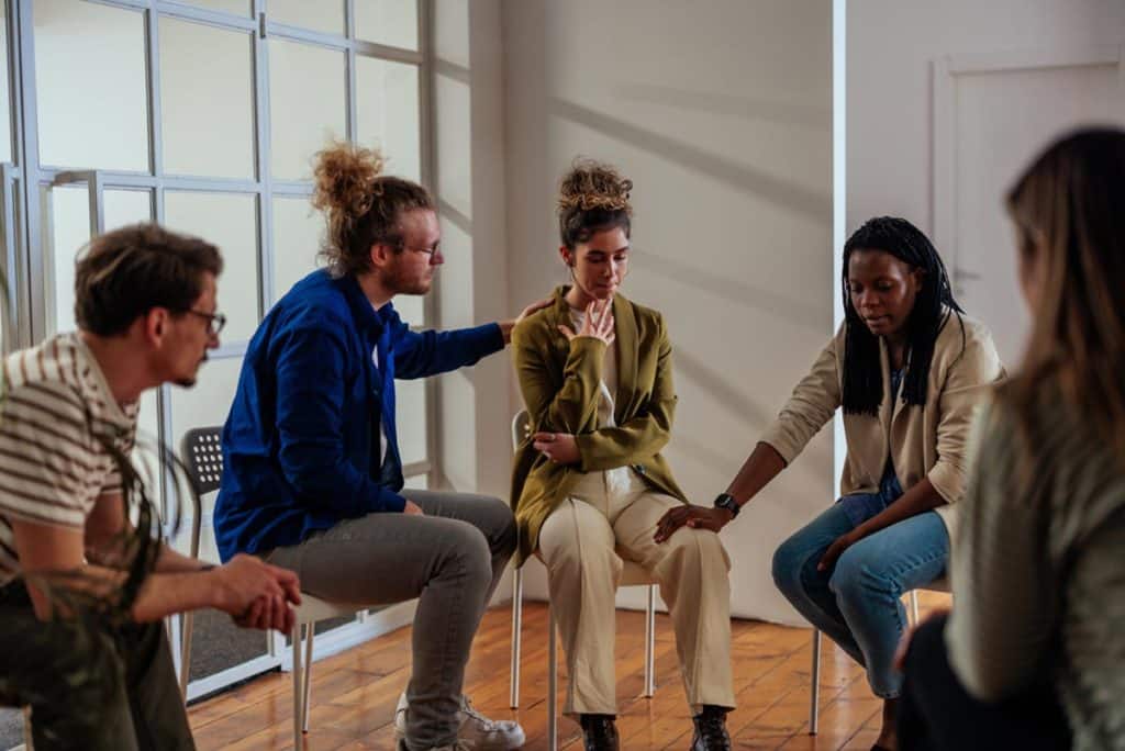 Group therapy members sitting in chair and consoling one another about alcohol recovery