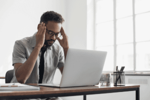 man seated in office in front of computer and rubbing his temples while wondering how does depression affect your work