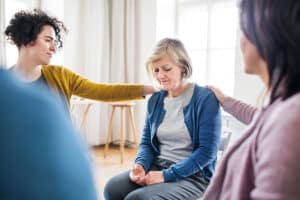 two members of a drug rehab program group session consoling a third member