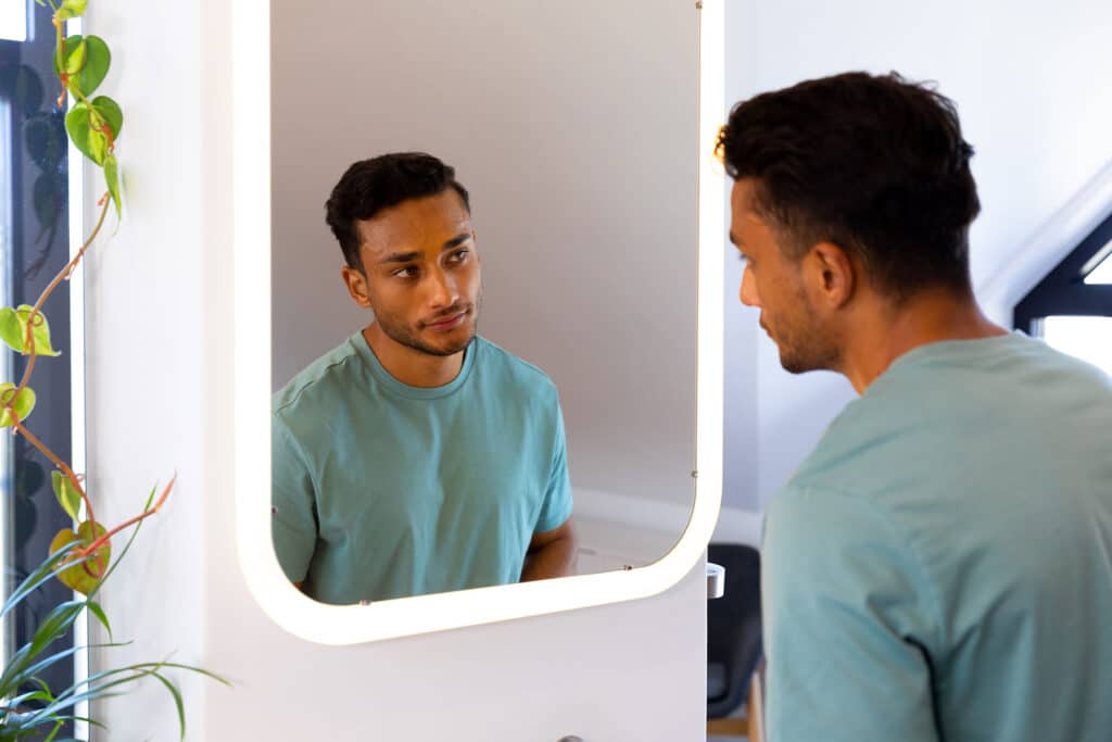 young man staring into mirror wondering what are the benefits of dual diagnosis treatment