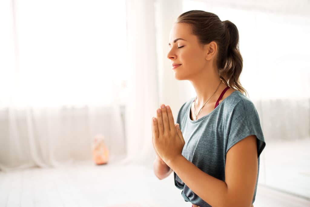 young woman standing with palms pressed together in meditative pose discovering what are the benefits of meditative therapy