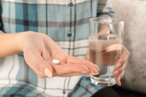 image of person with pain pill in one hand and glass of water in the other wondering what types of painkillers are addictive