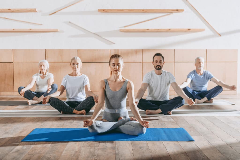 group of men and women engaged in a yoga class discovering what is yoga therapy for behavioral health