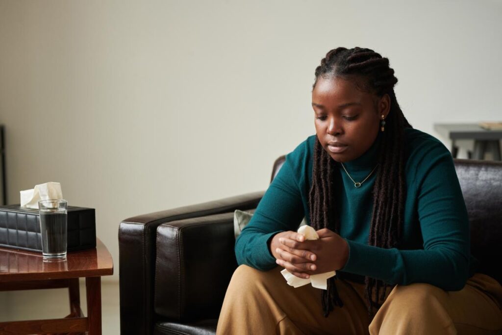 young woman looking concerned as she sits on couch in office and wonders what is the best treatment for PTSD?