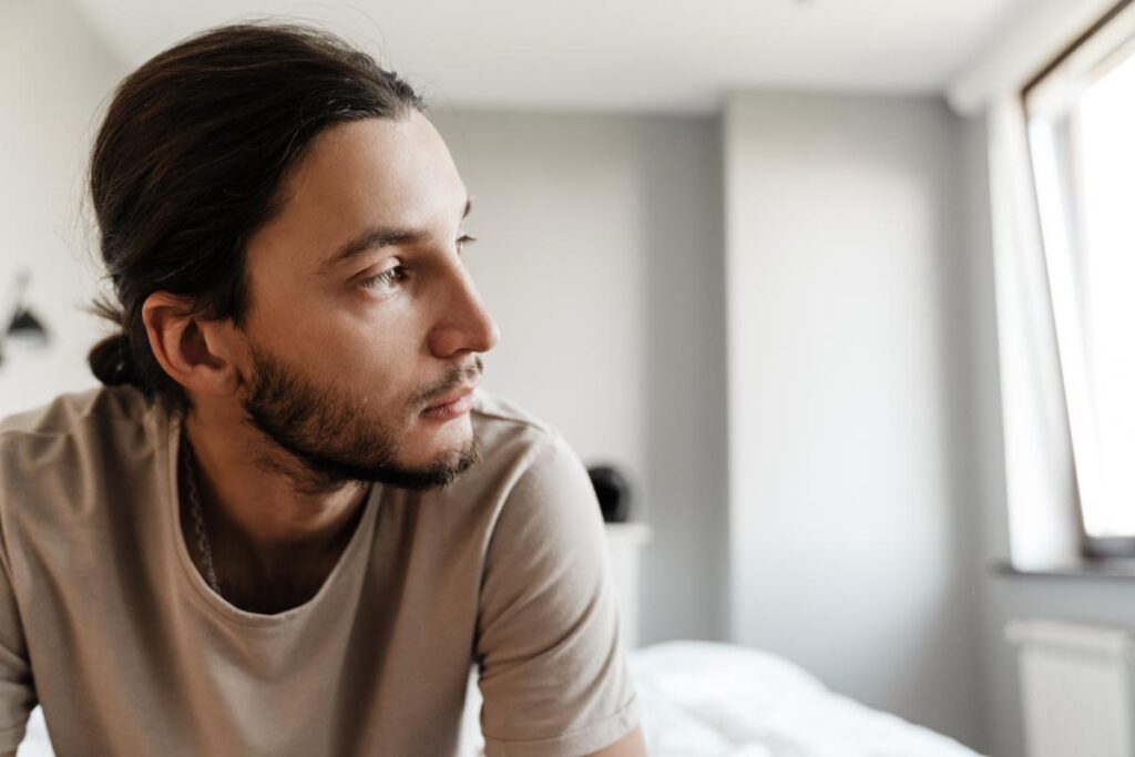 young man seated on his bed looking anxious as he ponders the 3 signs of cocaine addiction