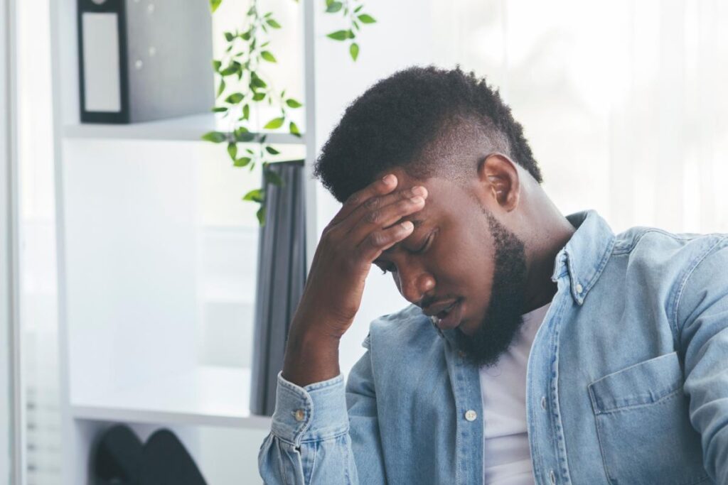 troubled young man seated on couch with head in his hands contemplating heroin addiction and when to get help.