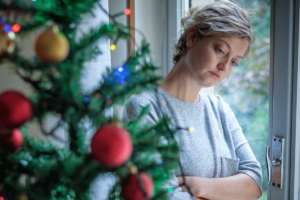 woman sitting by window with Christmas tree contemplating the various tips on relieving holiday stress