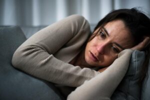 young woman looking anxious and distraught while curled up on couch wondering when to do an alcohol detox