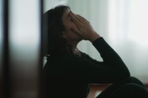 young woman in dimly lit room seated on floor and leaning against wall experiencing one of 6 signs of bipolar disorder in a loved one