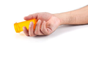 the hand of a presumably unconscious individual holds an empty pill bottle