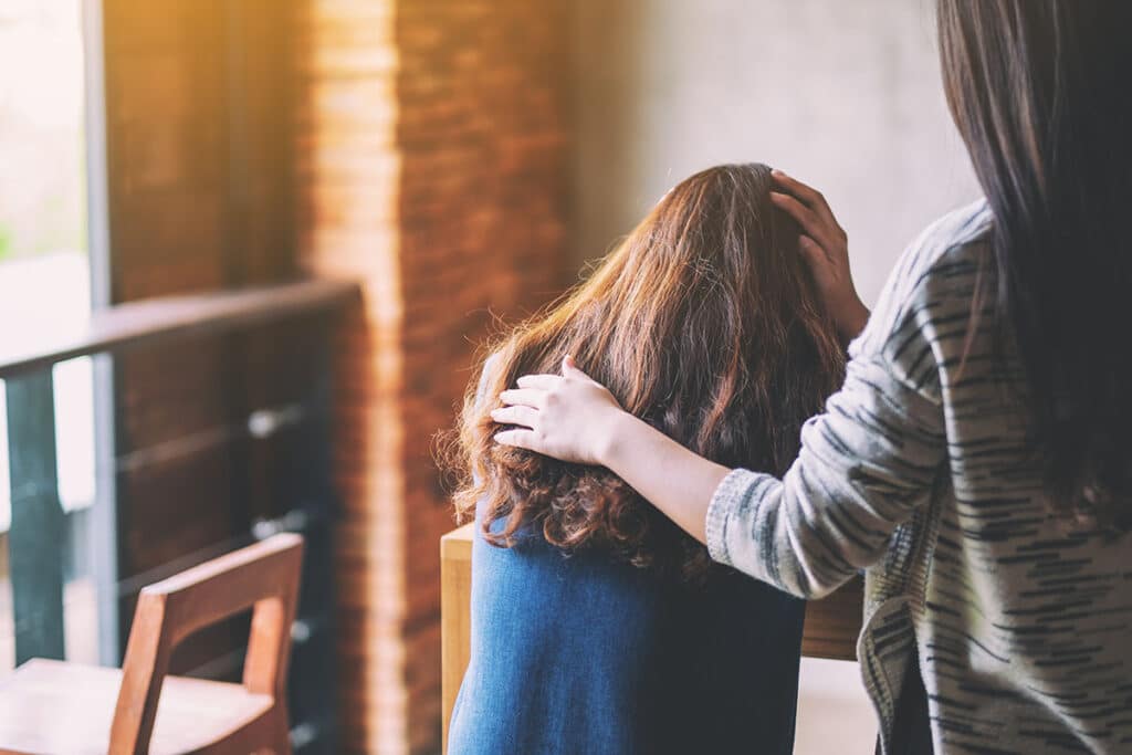 young woman exhibiting one of 5 sings of painkiller withdrawal being consoled and supported by older adult female.